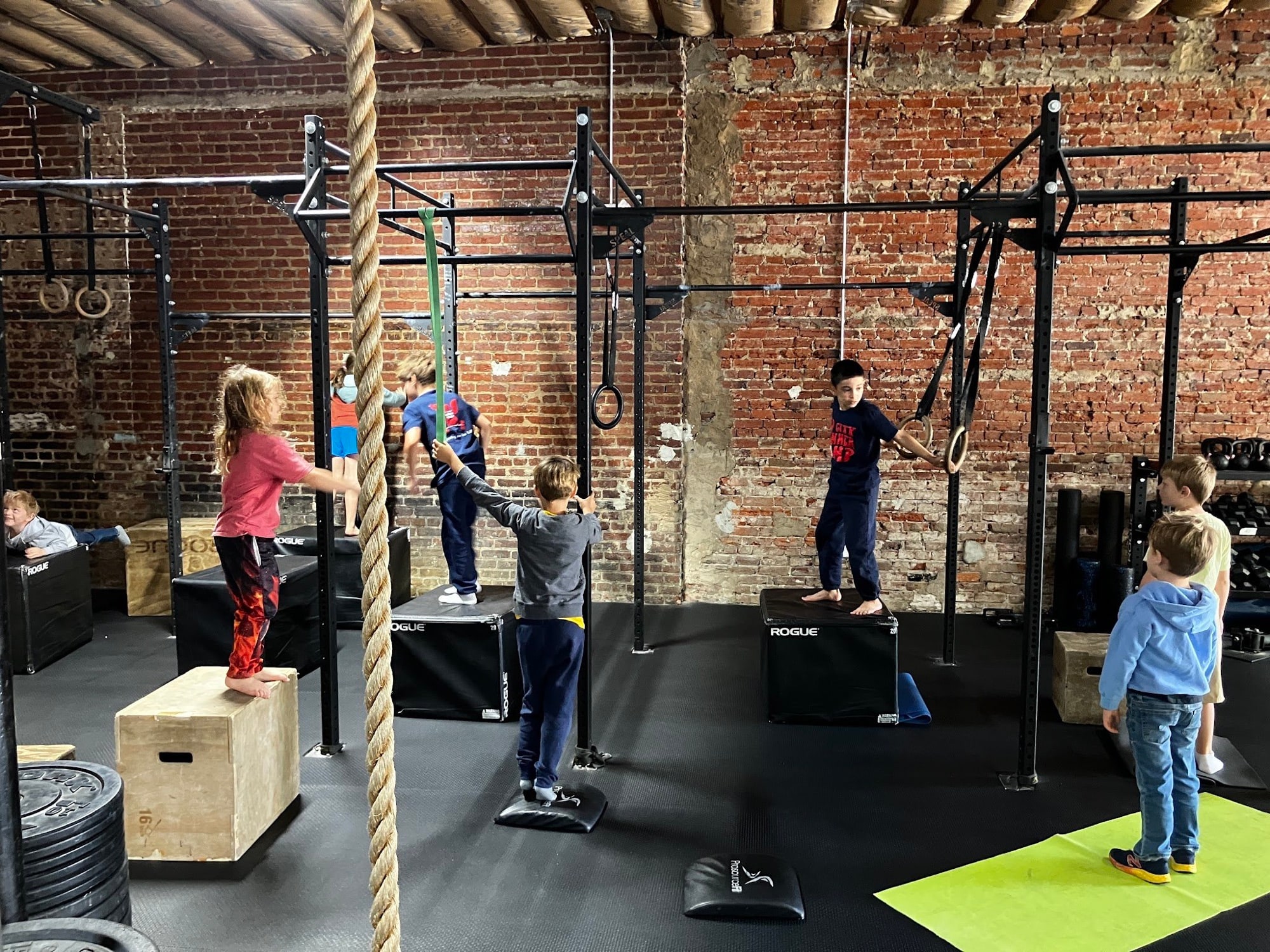Kids training in the gym — a girl jumping onto a box, a boy on gymnastic rings